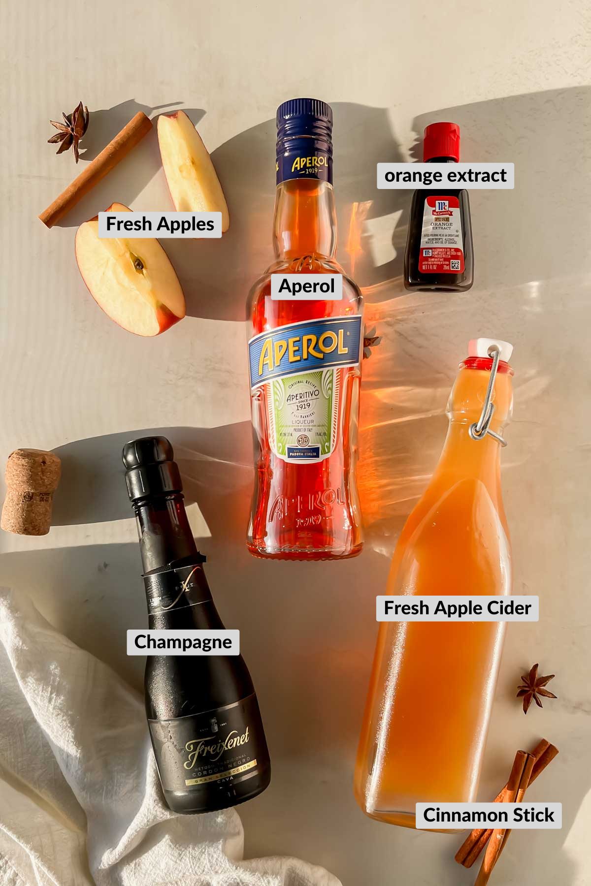 labeled apple cider aperol spritz ingredients spread on plain background.