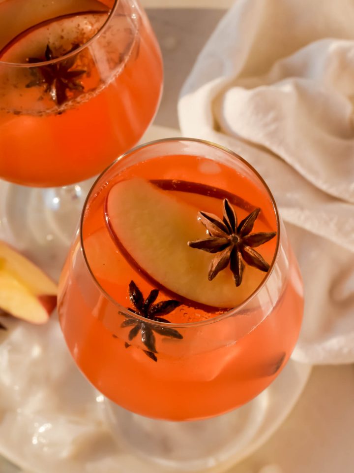 apple cider spritz in a wine glass garnished with apple slices and star anise.