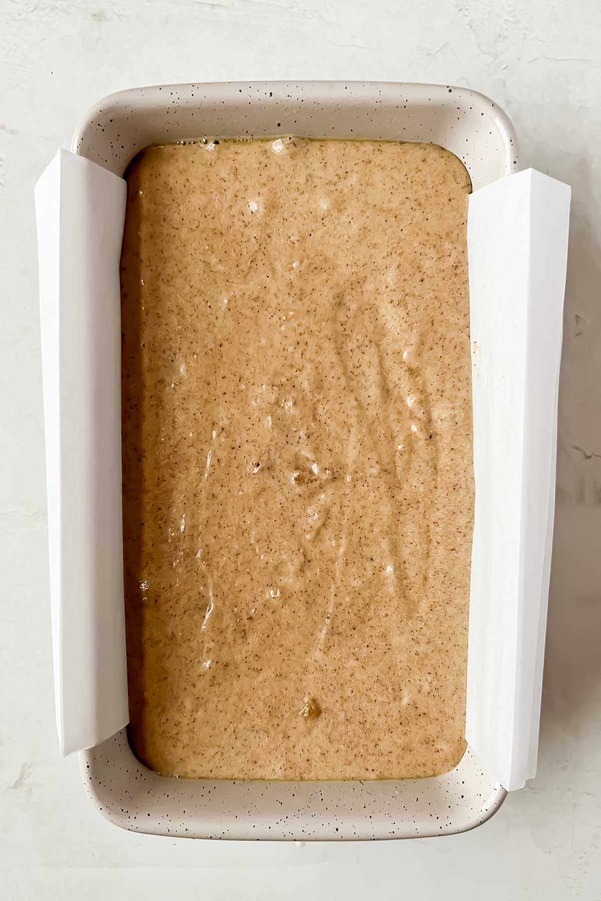 cinnamon donut bread batter in parchment lined loaf pan before baking.
