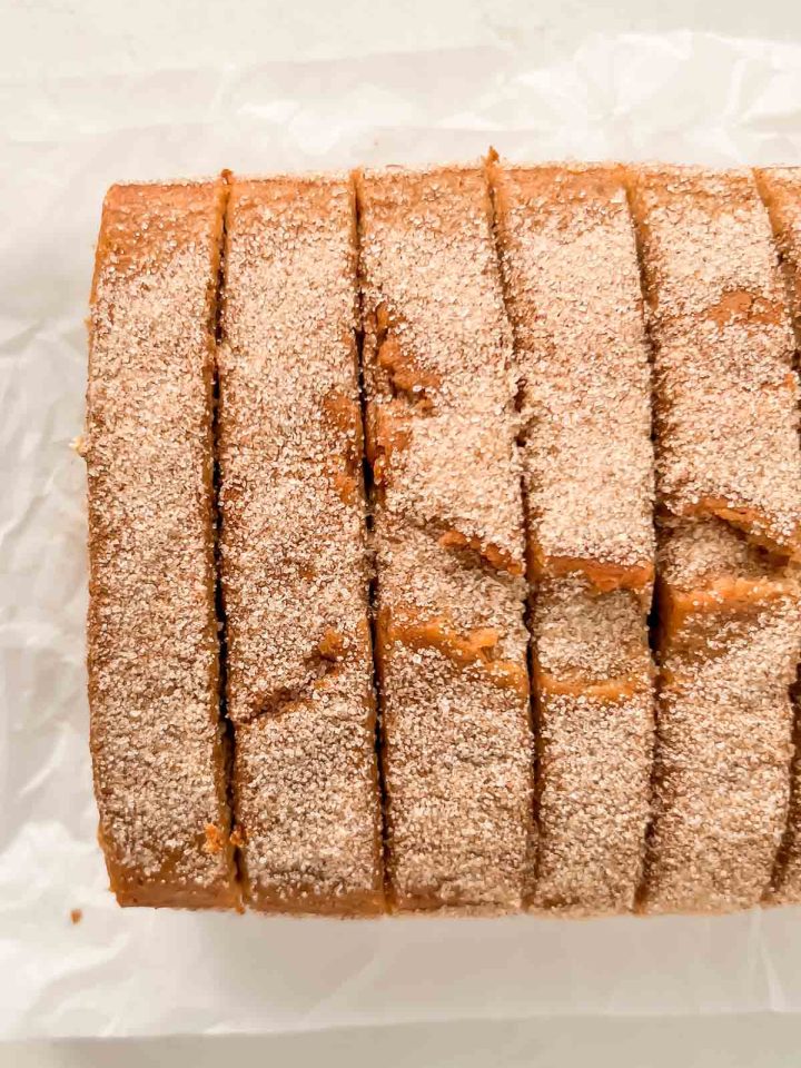 sliced cinnamon donut bread dusted with cinnamon sugar on white parchment paper.