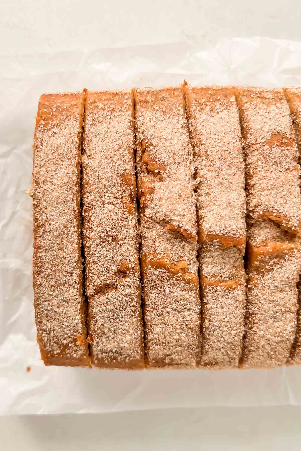 sliced cinnamon donut bread dusted with cinnamon sugar on white parchment paper.