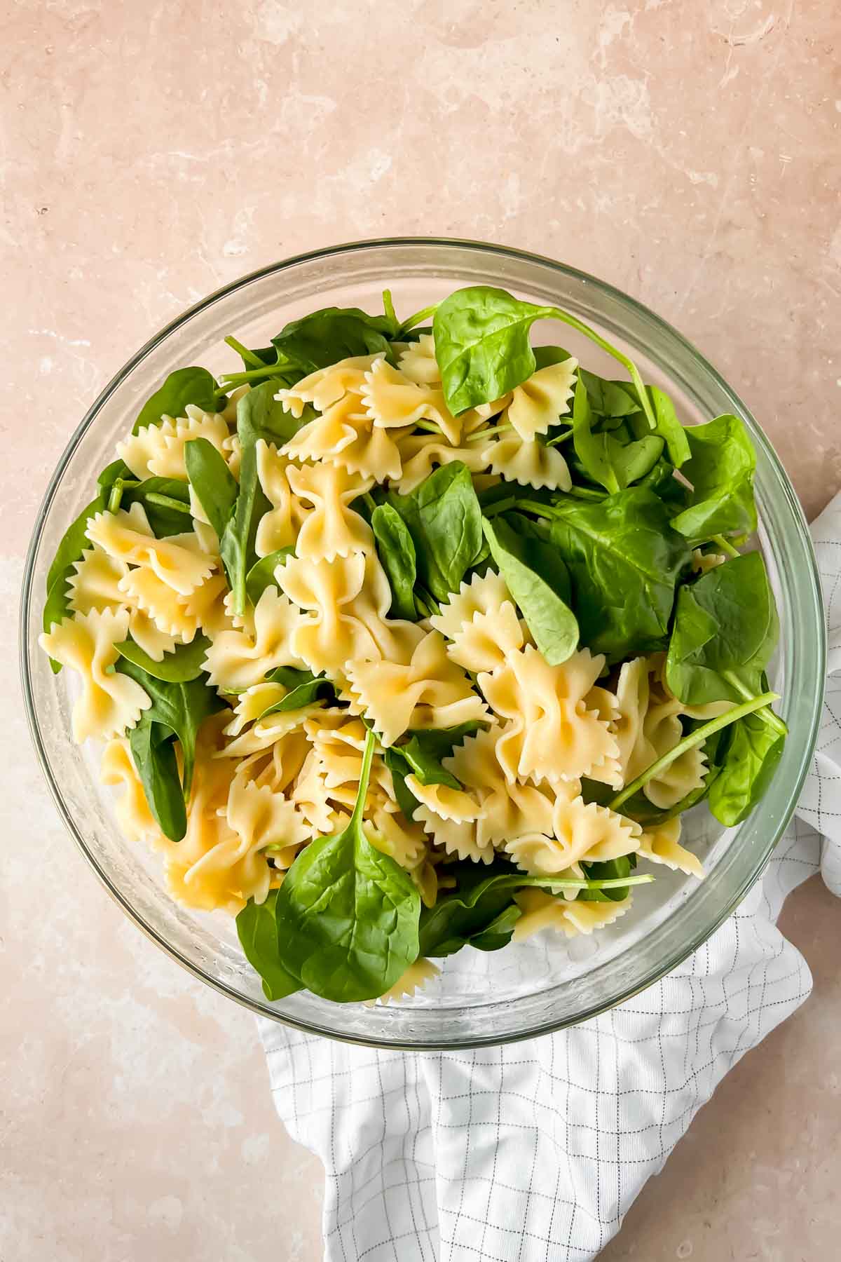 bowtie noodles and spinach in glass mixing bowl.