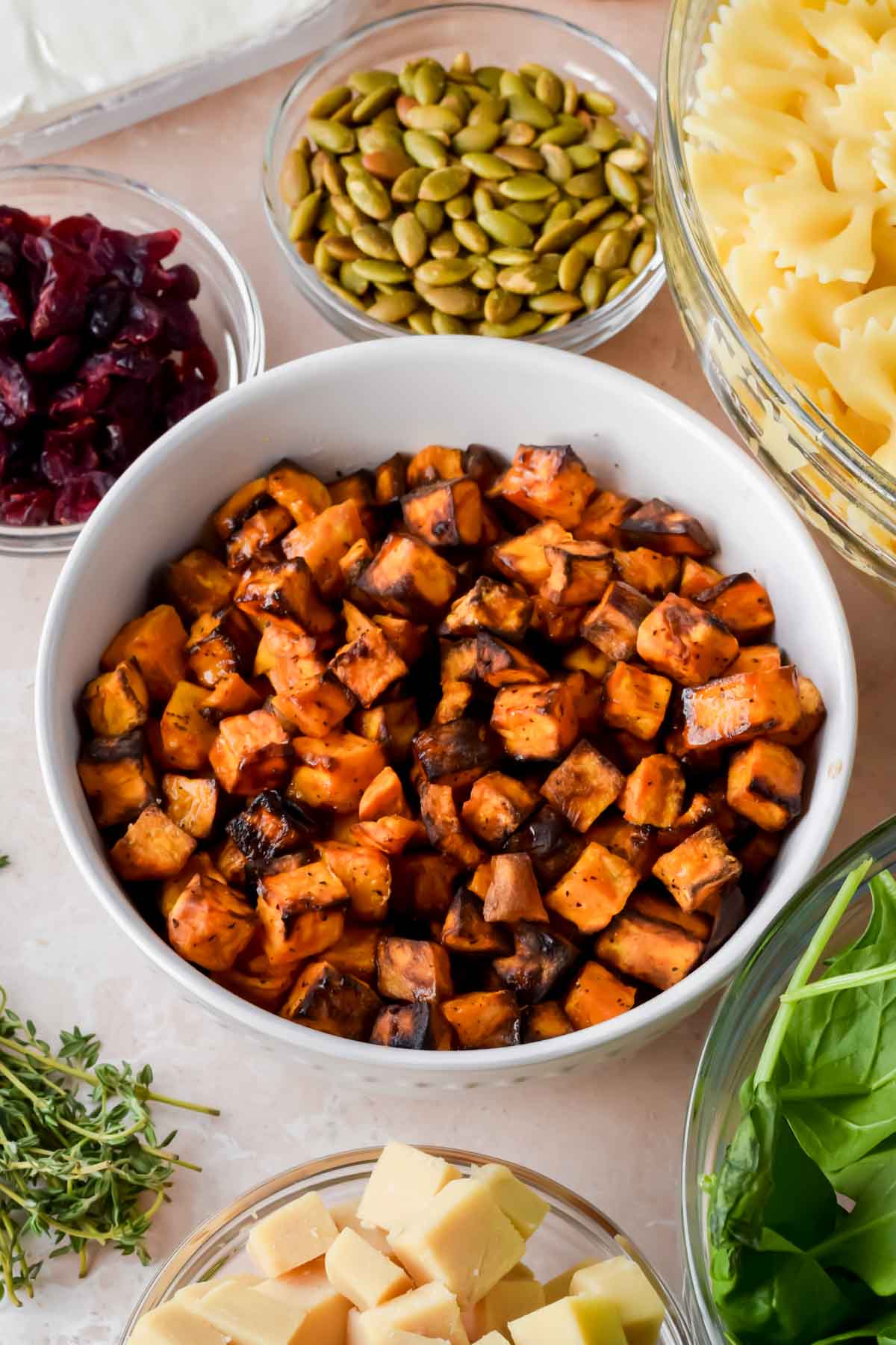 roasted sweet potato cubes in white bowl surrounded by additional ingredients for fall pasta salad.