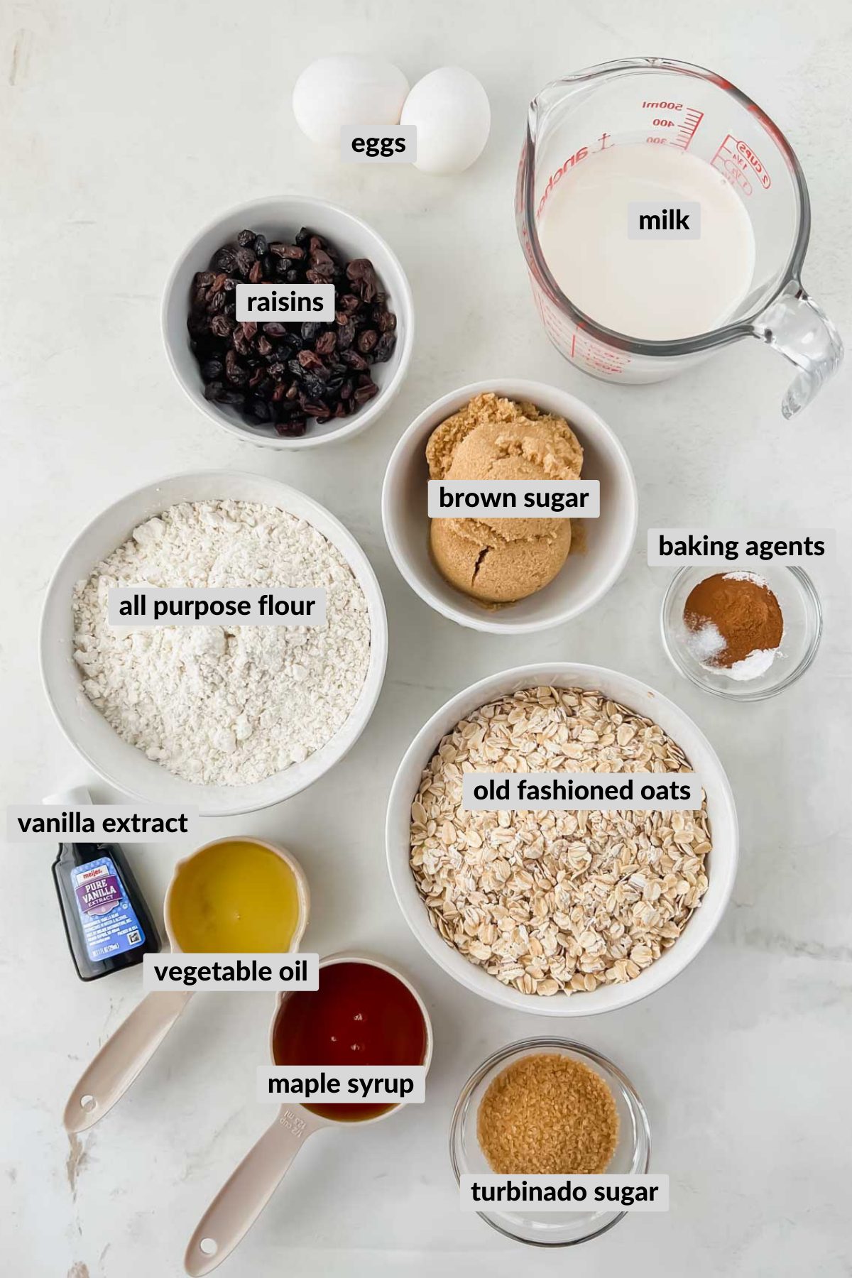 ingredients for oatmeal raisin muffins in individual bowls on white background.