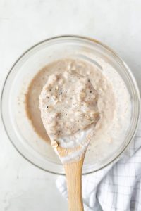 overnight oats ingredients mixed in glass bowl and scooped on wooden spoon.