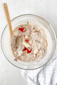 overnight oats ingredients mixed in glass bowl with diced pear mixed in.