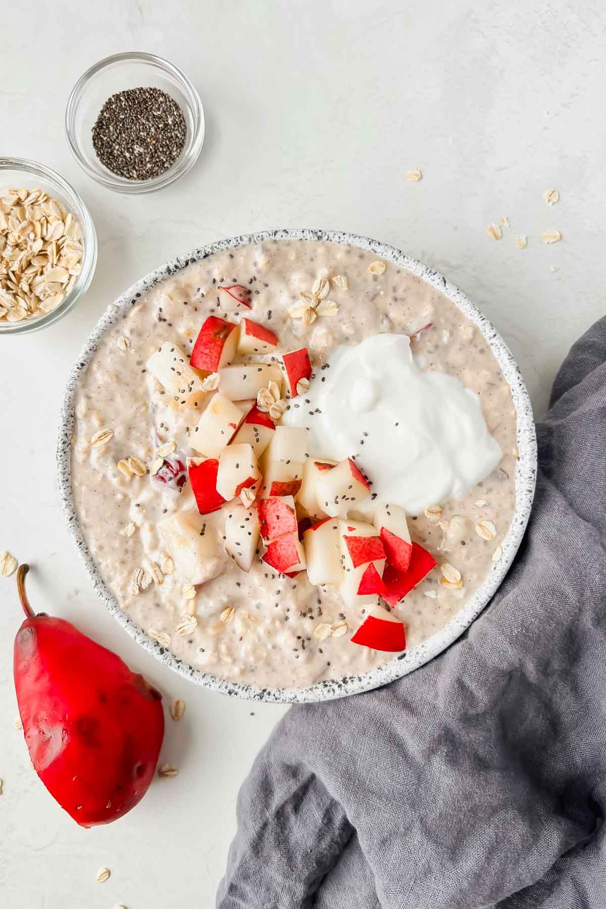 pear overnight oats in bowl topped with diced red pear, chia seeds and yogurt.
