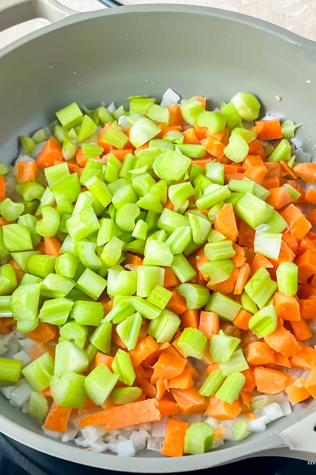 onions, carrots, and celery in gray skillet.
