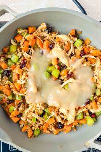 onions, carrots, celery, cranberries, and shredded turkey topped with gravy in gray skillet.