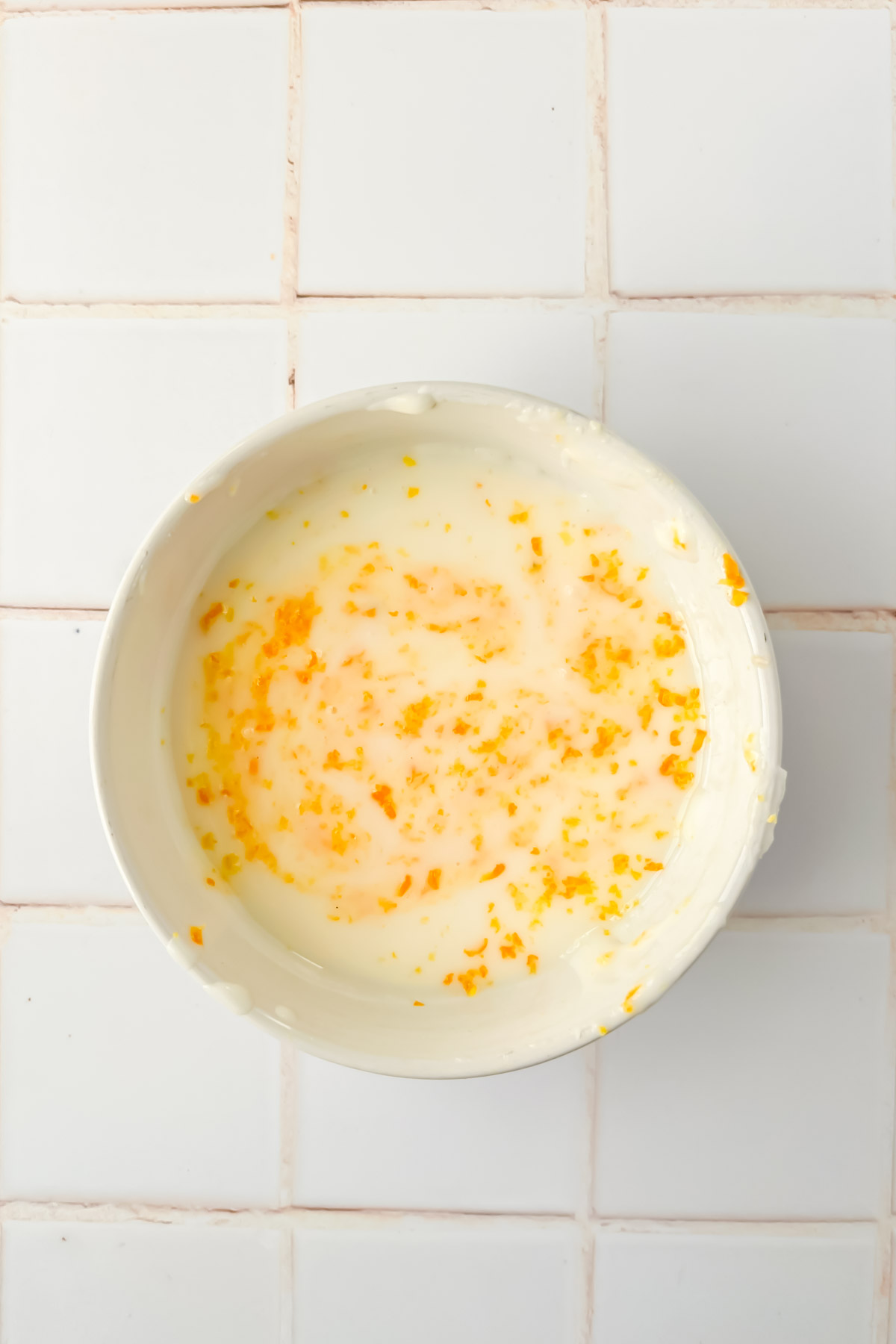white glaze with orange zest mixed in in white mixing bowl.