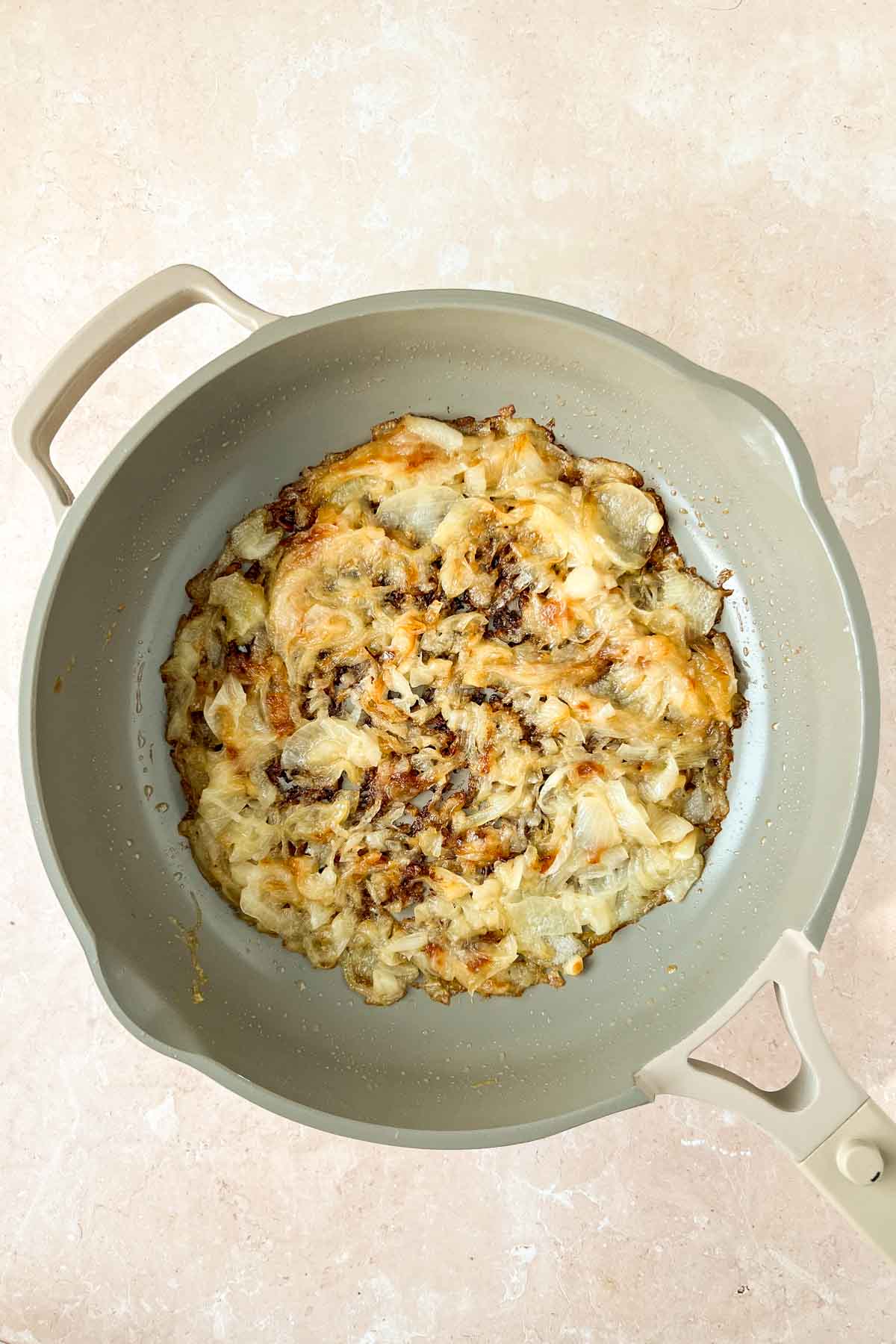 caramelized onions in gray skillet with grated cheese mixed in.