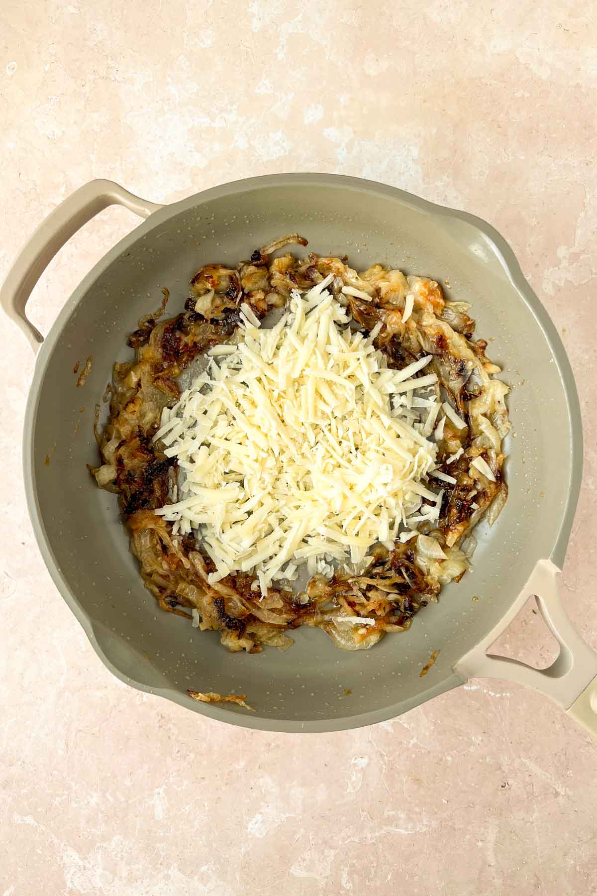 caramelized onions in gray skillet with grated cheese added on top.
