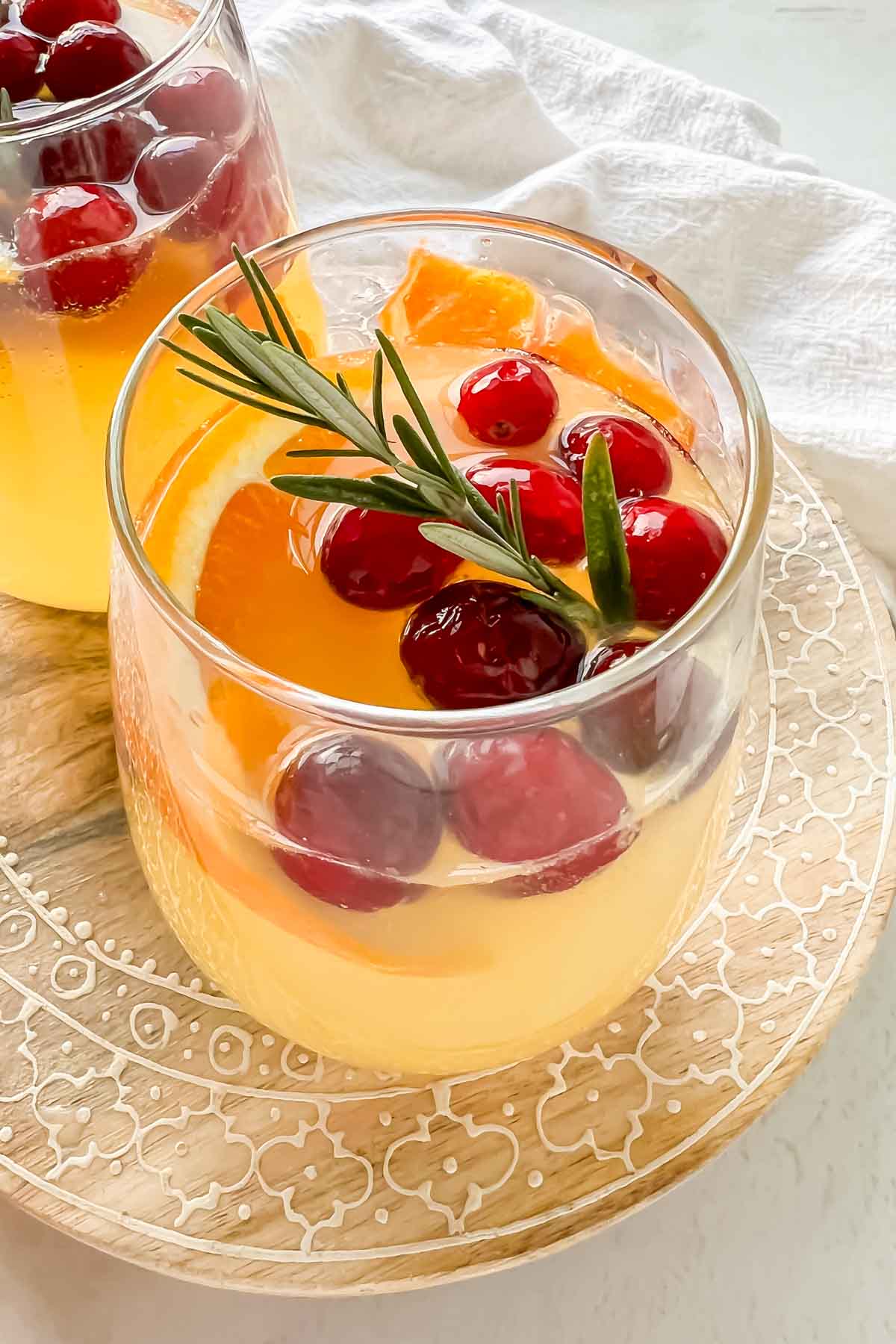 white wine sangria with vodka in stemless wine glass garnished with orange slice, cranberries and rosemary.
