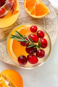 white wine sangria with vodka in stemless wine glass garnished with orange slice, cranberries and rosemary.