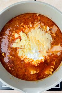 tomato based soup in gray pot topped with parmesan cheese flakes.