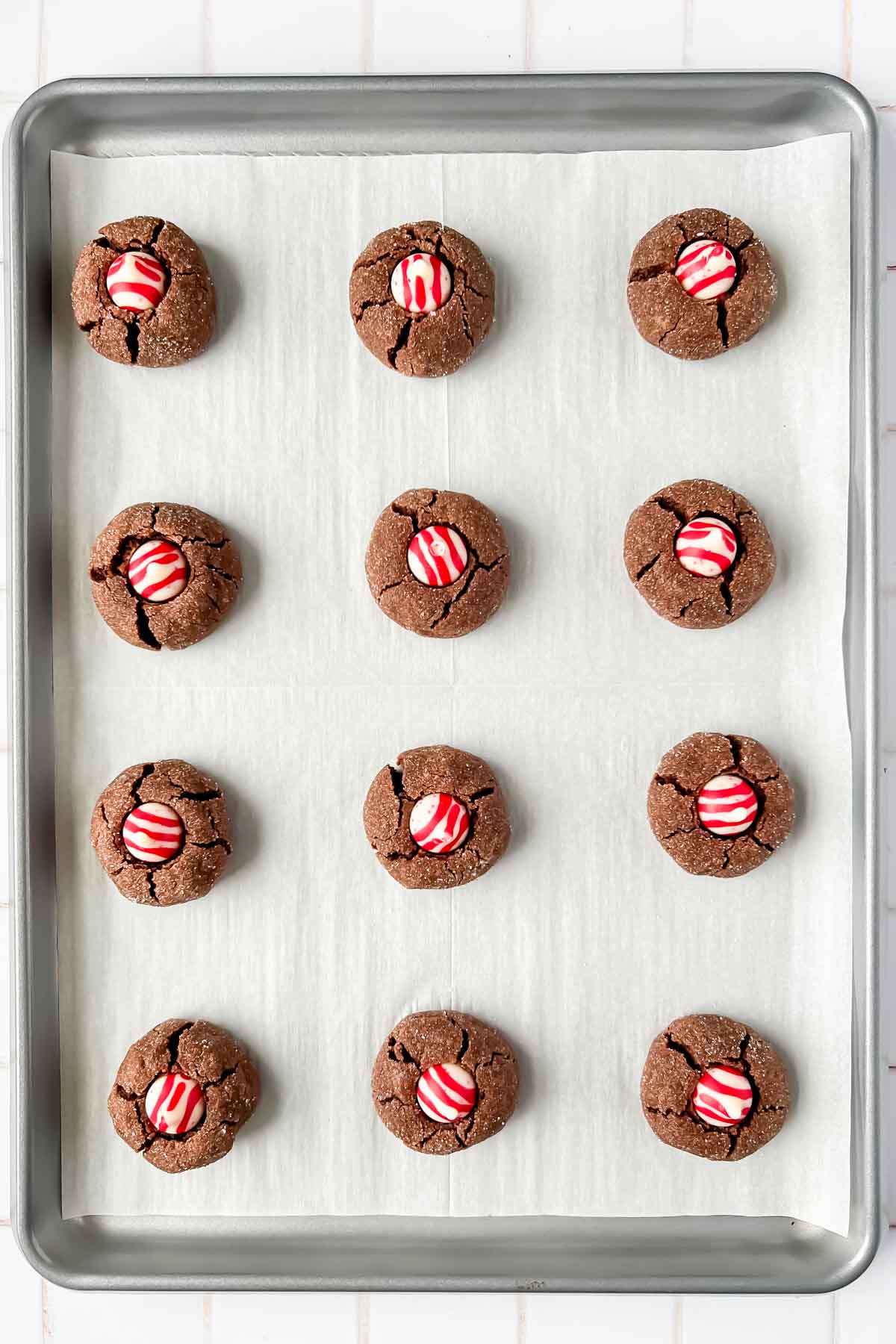 12 chocolate peppermint kiss cookies aligned on silver baking tray lined with parchment.