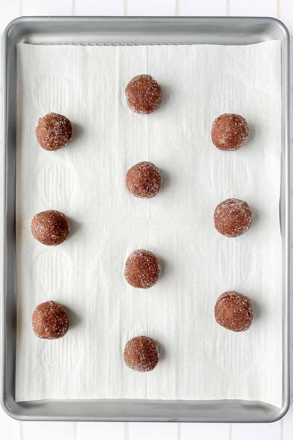 chocolate peppermint kiss cookie dough balls aligned on silver baking tray lined with parchment.