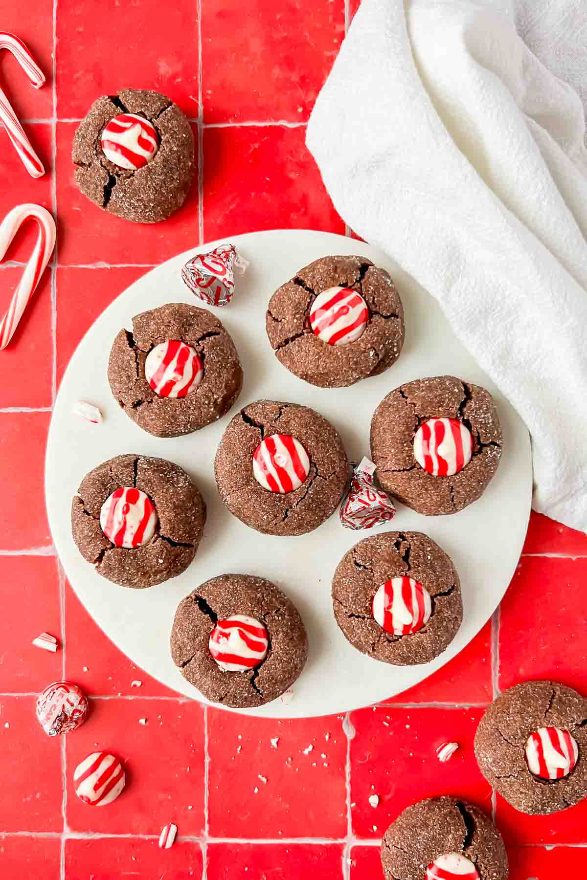 chocolate peppermint kiss cookies on white plate on red tile background.