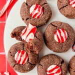 chocolate peppermint kiss cookies on white plate on red tile background.