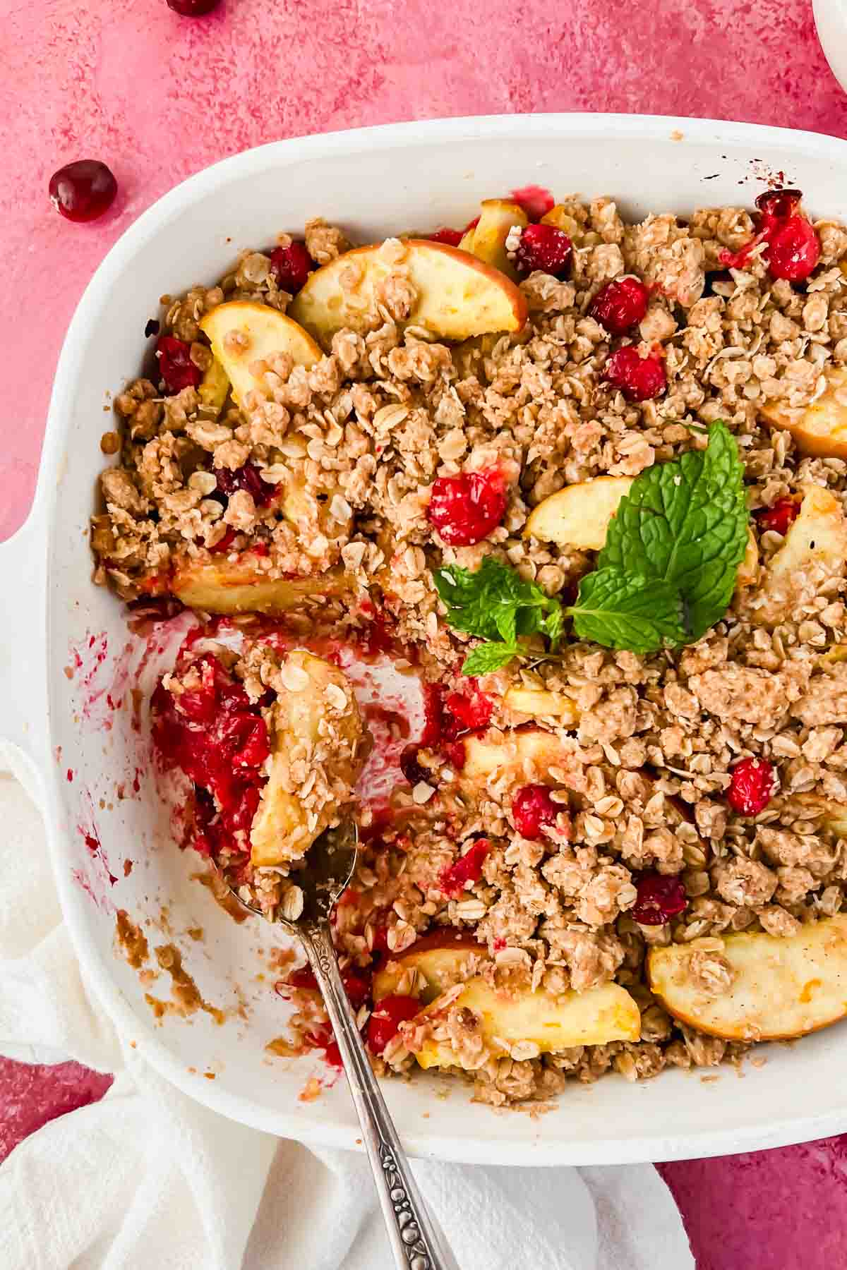 baked apple cranberry crisp with a spoonful taken out on red background. 