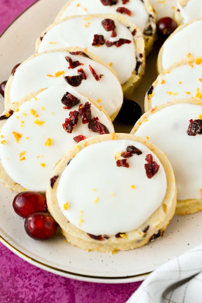 cranberry orange shortbread cookies with white frosting on speckled serving plate.
