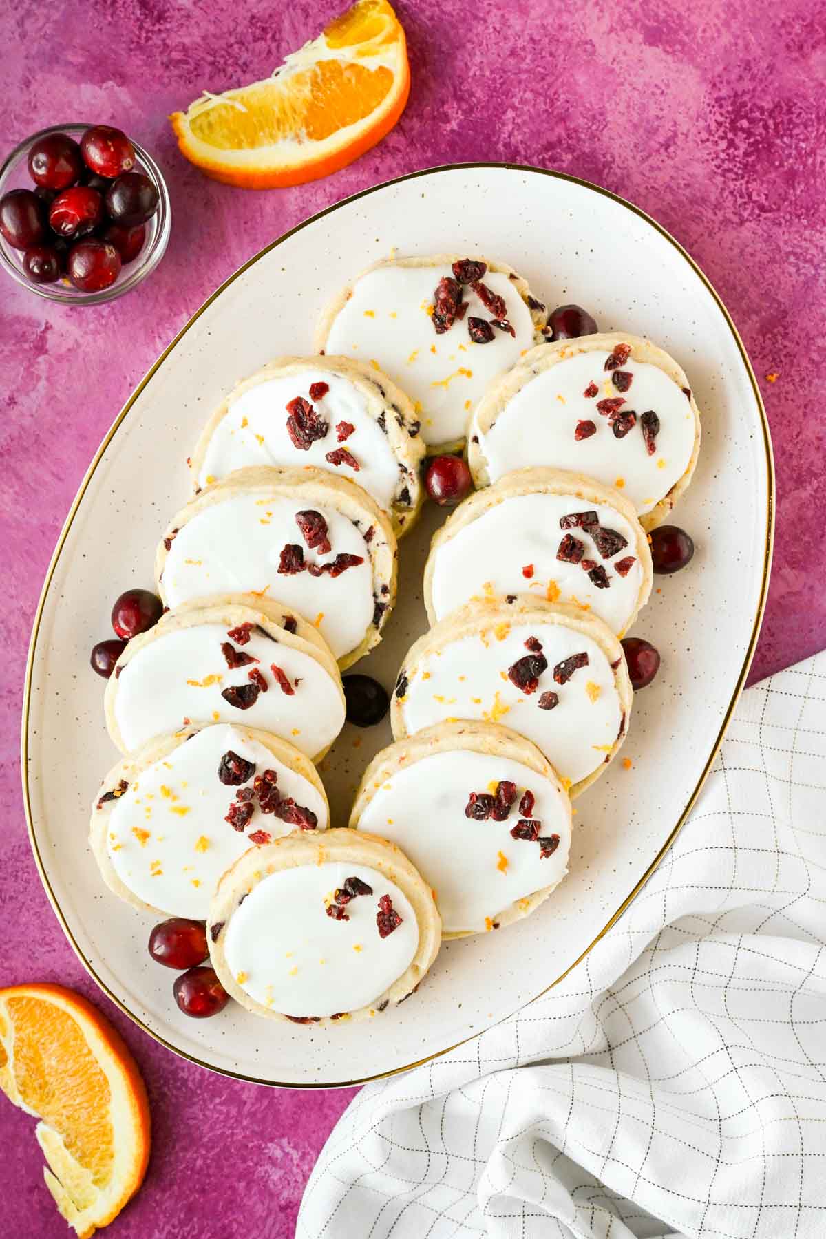cranberry orange shortbread cookies with white frosting on speckled serving plate.