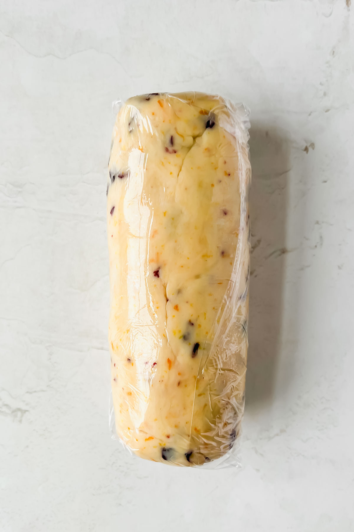 cranberry orange shortbread cookie dough rolled into log wrapped with clear plastic wrap.