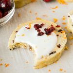 cranberry orange shortbread cookie with white frosting with bite taken out of it.