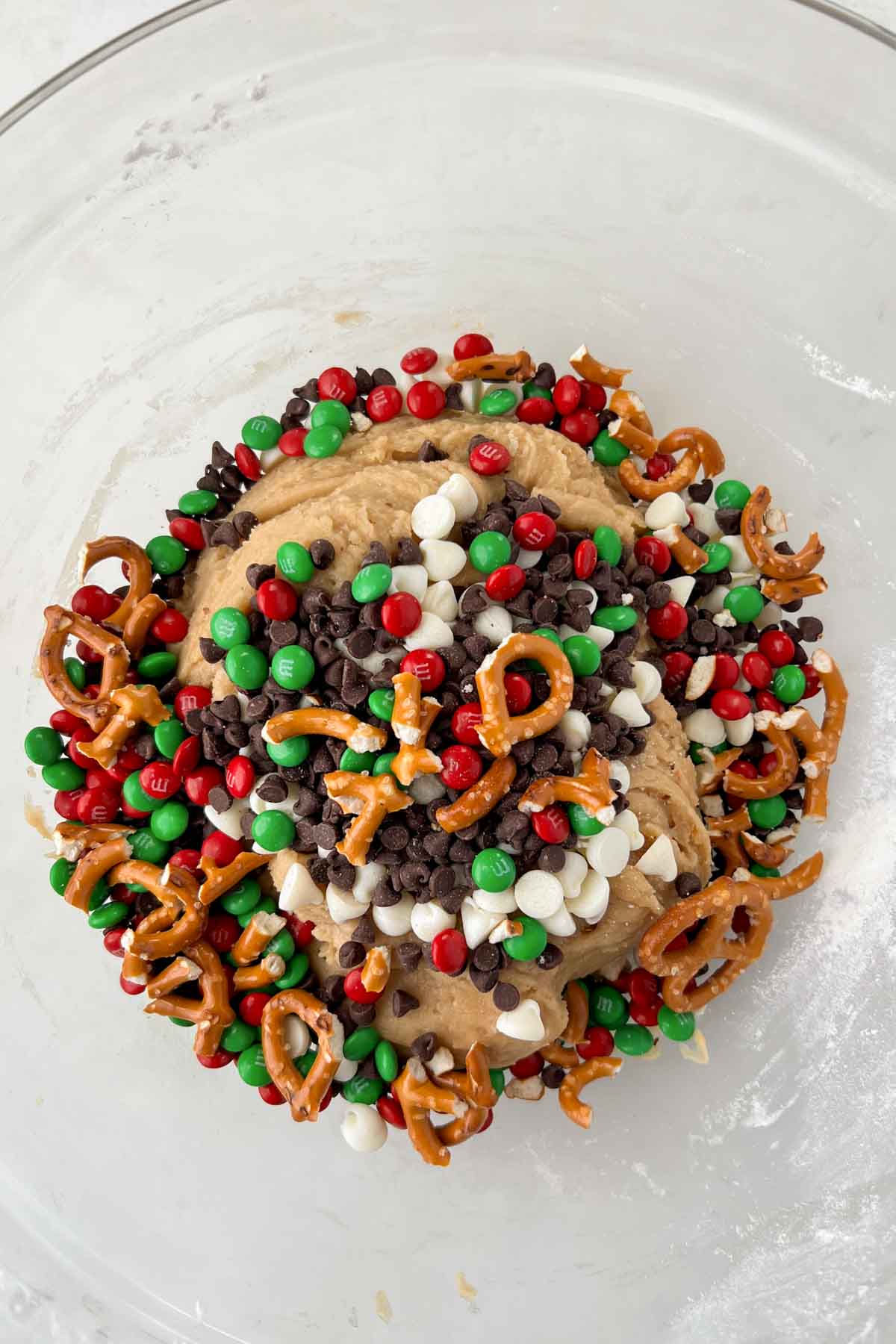 kitchen sink christmas cookie dough topped with all of the mix ins in glass mixing bowl.