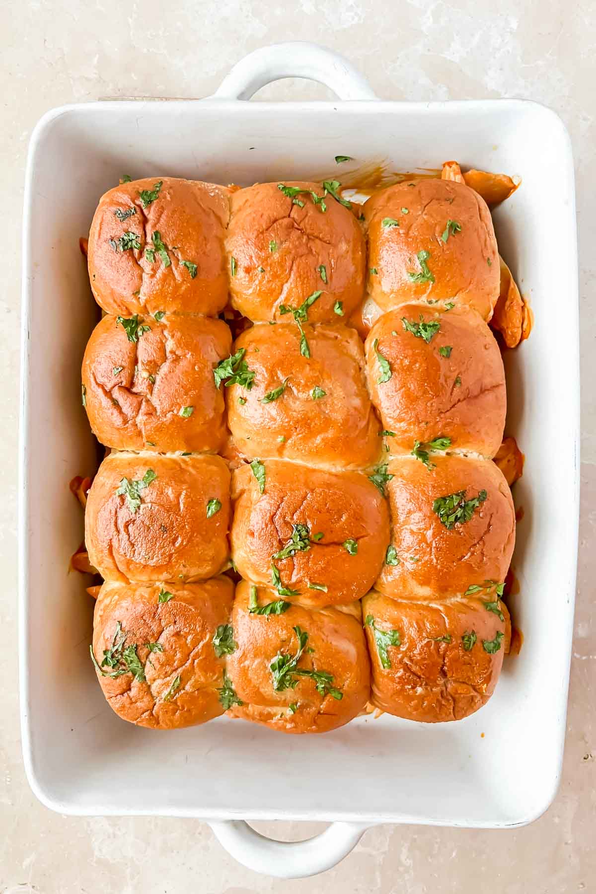 pan full of buffalo chicken sliders garnished with fresh herbs.