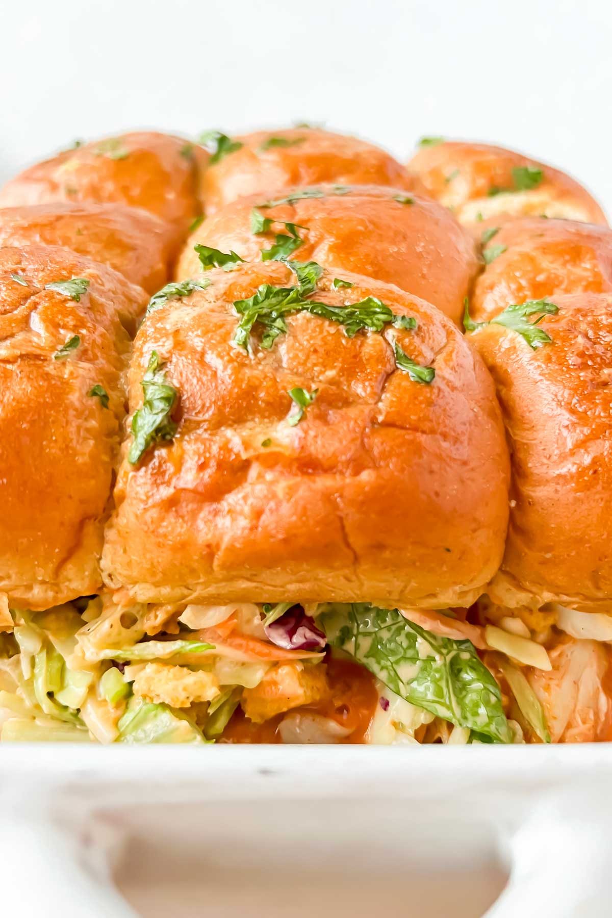 pan full of buffalo chicken sliders garnished with fresh herbs.