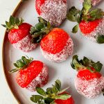champagne soaked strawberries dipped in sugar aligned on white plate.