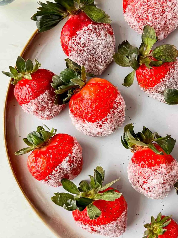 champagne soaked strawberries dipped in sugar aligned on white plate.