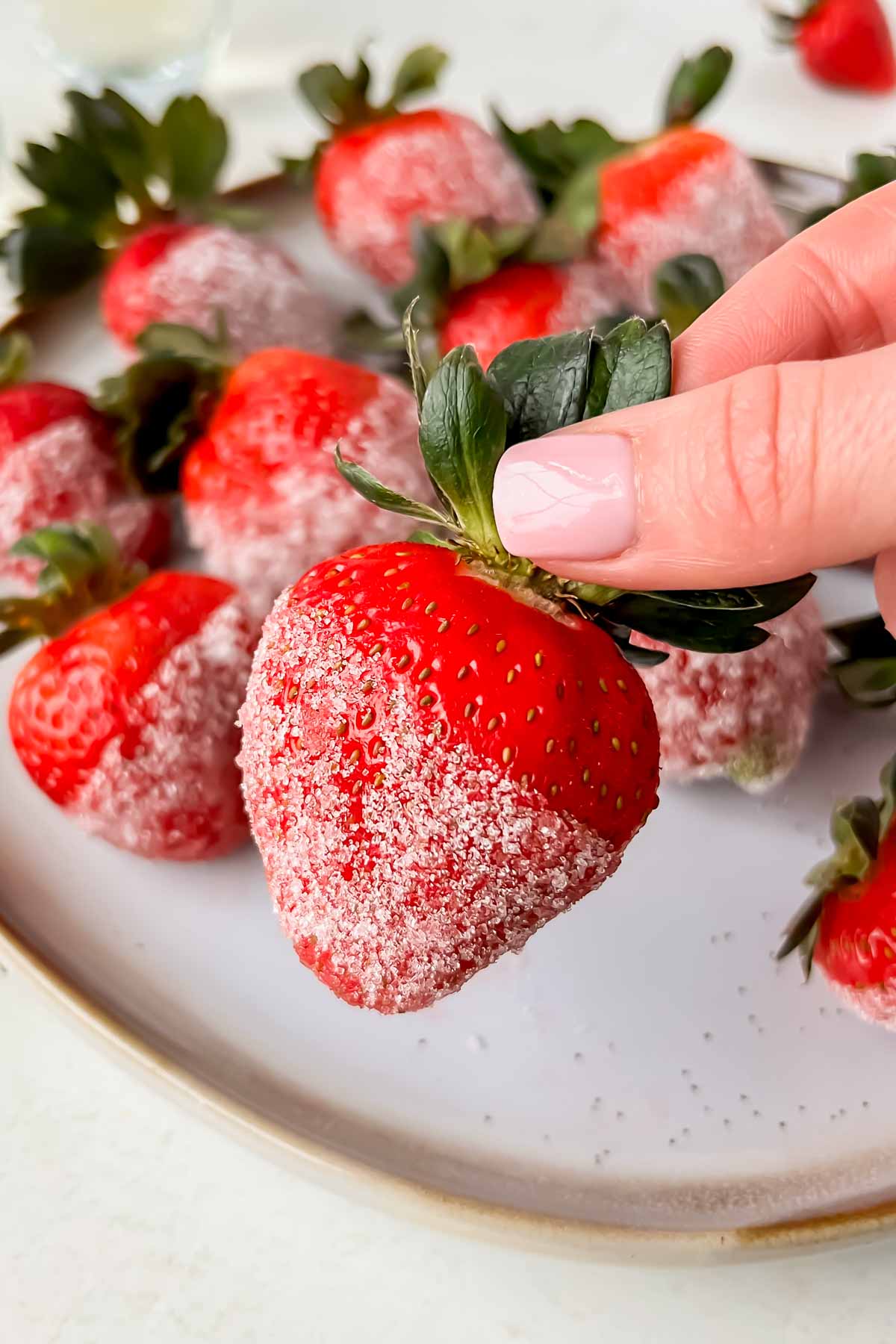 hand grabbing champagne soaked strawberry dipped in sugar.