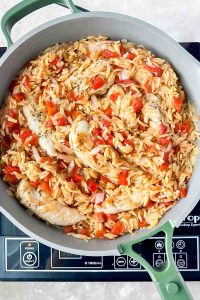 chicken with tomatoes and orzo cooked together in gray skillet.