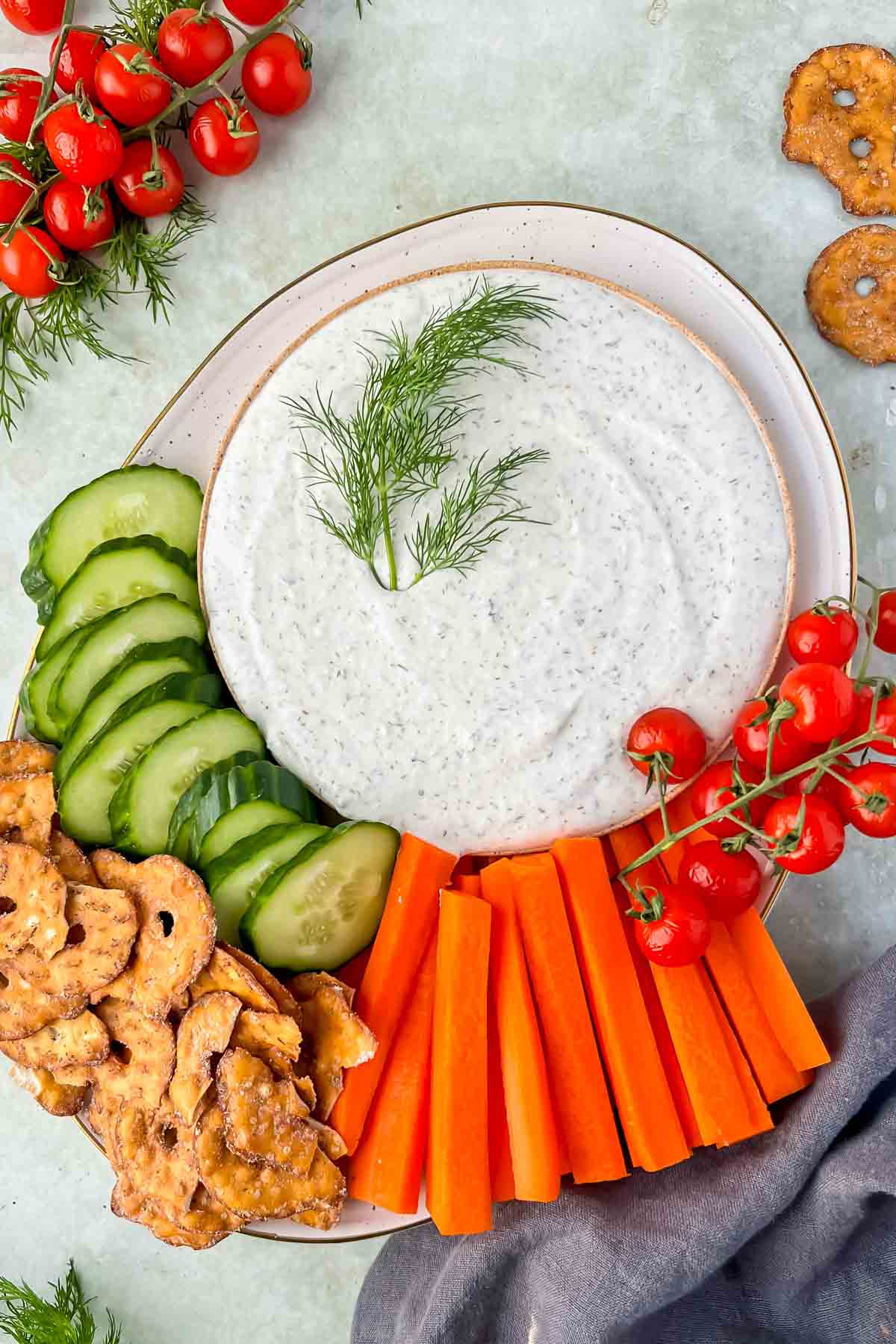 cottage cheese ranch dip with fresh dill as garnish on plate with cucumbers, carrots and pretzels.