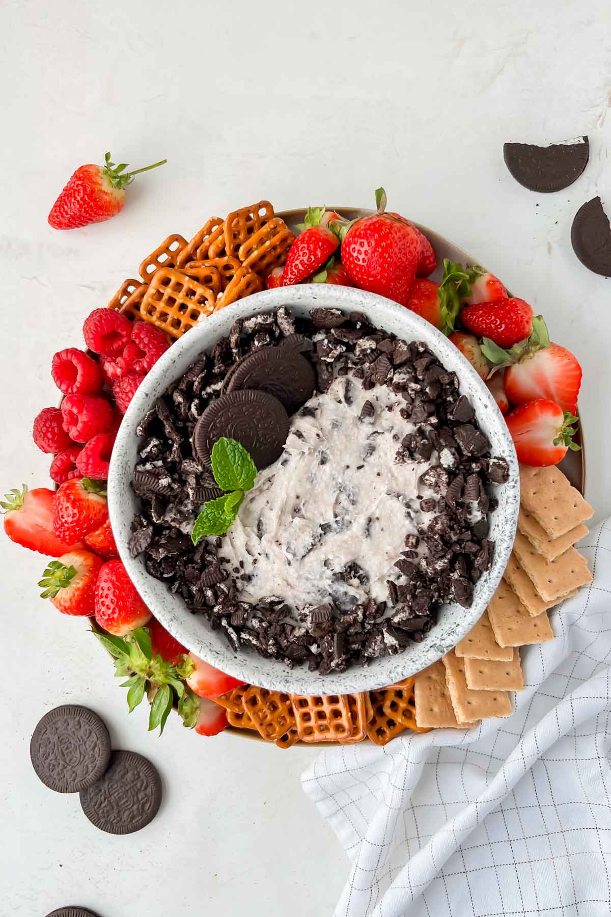 oreo dip in white serving bowl on plate with strawberries, raspberries, pretzels, and graham crackers.