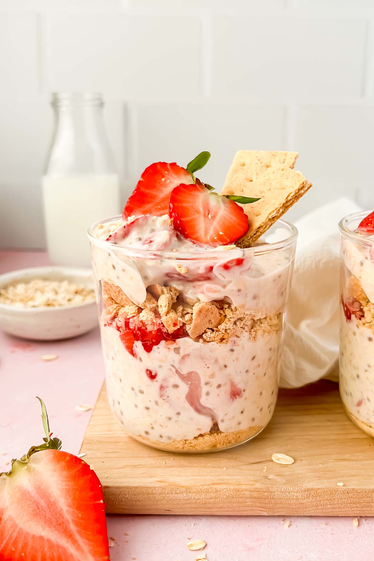 glass cup full of strawberry cheesecake overnight oats garnished with fresh strawberries and graham crackers.