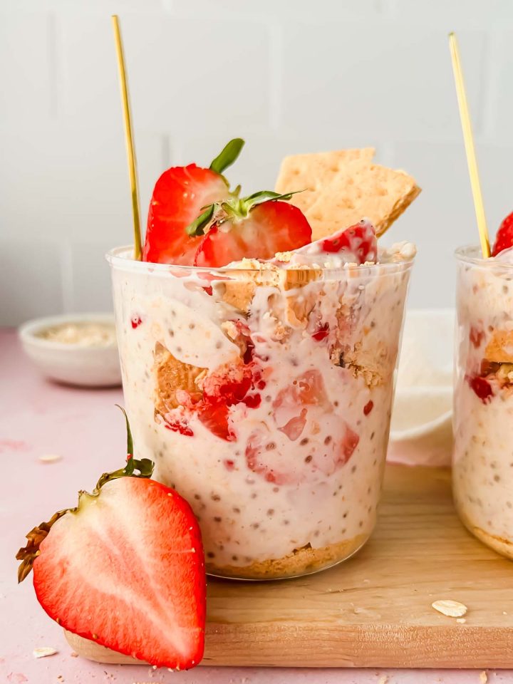 glass cup full of strawberry cheesecake overnight oats garnished with fresh strawberries and graham crackers.