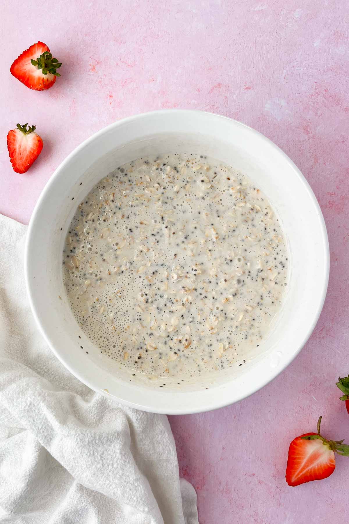strawberry cheesecake overnight oats ingredients mixed in white bowl with extra strawberries and graham crackers on top.