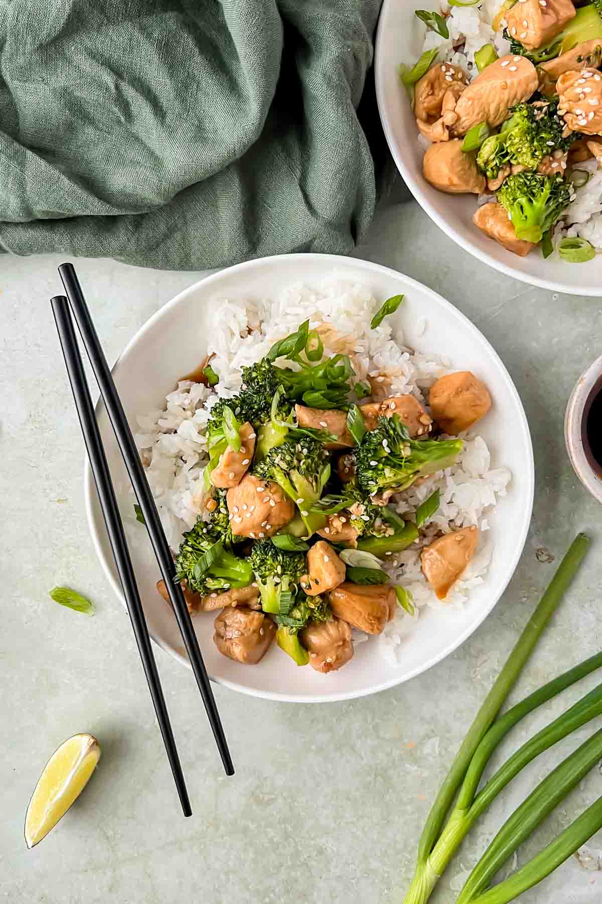 teriyaki chicken and broccoli served over white rice in white bowl with chopsticks.