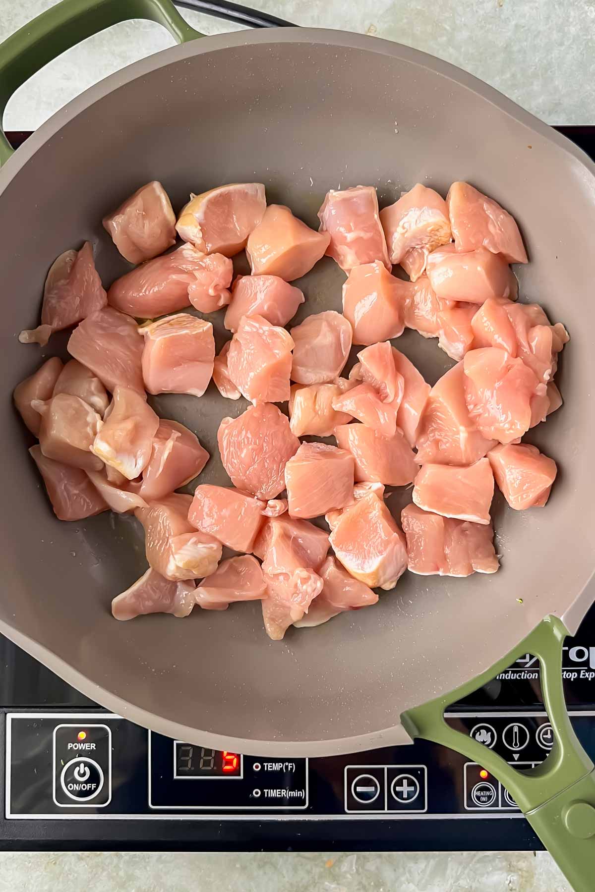 raw chicken cut into cubes added to gray skillet.