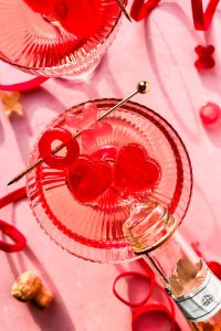 pouring a glass of rosé into couple glass with two pink jello hearts and garnished with a cocktail stick.