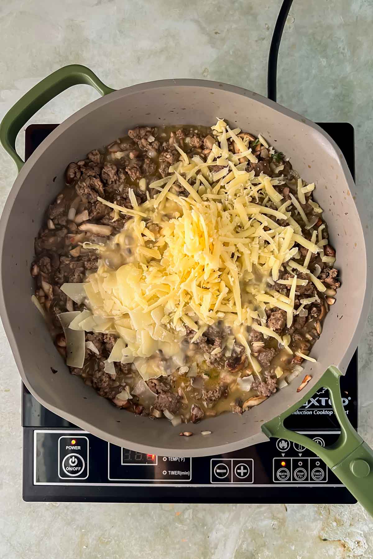 ground sausage and veggies cooking in gray skillet topped with shredded cheese.