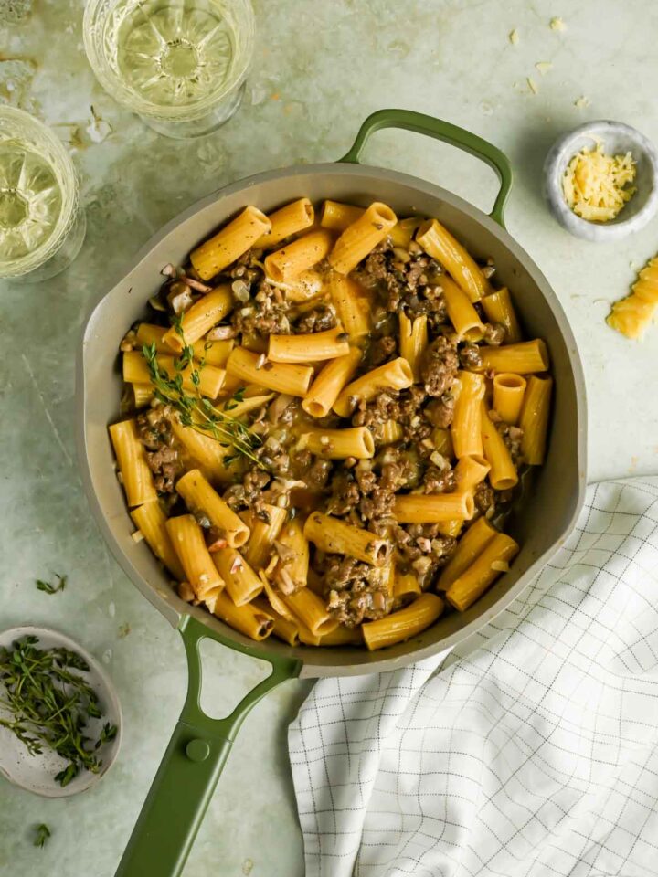sausage mushroom pasta topped with fresh thyme in green and gray skillet.