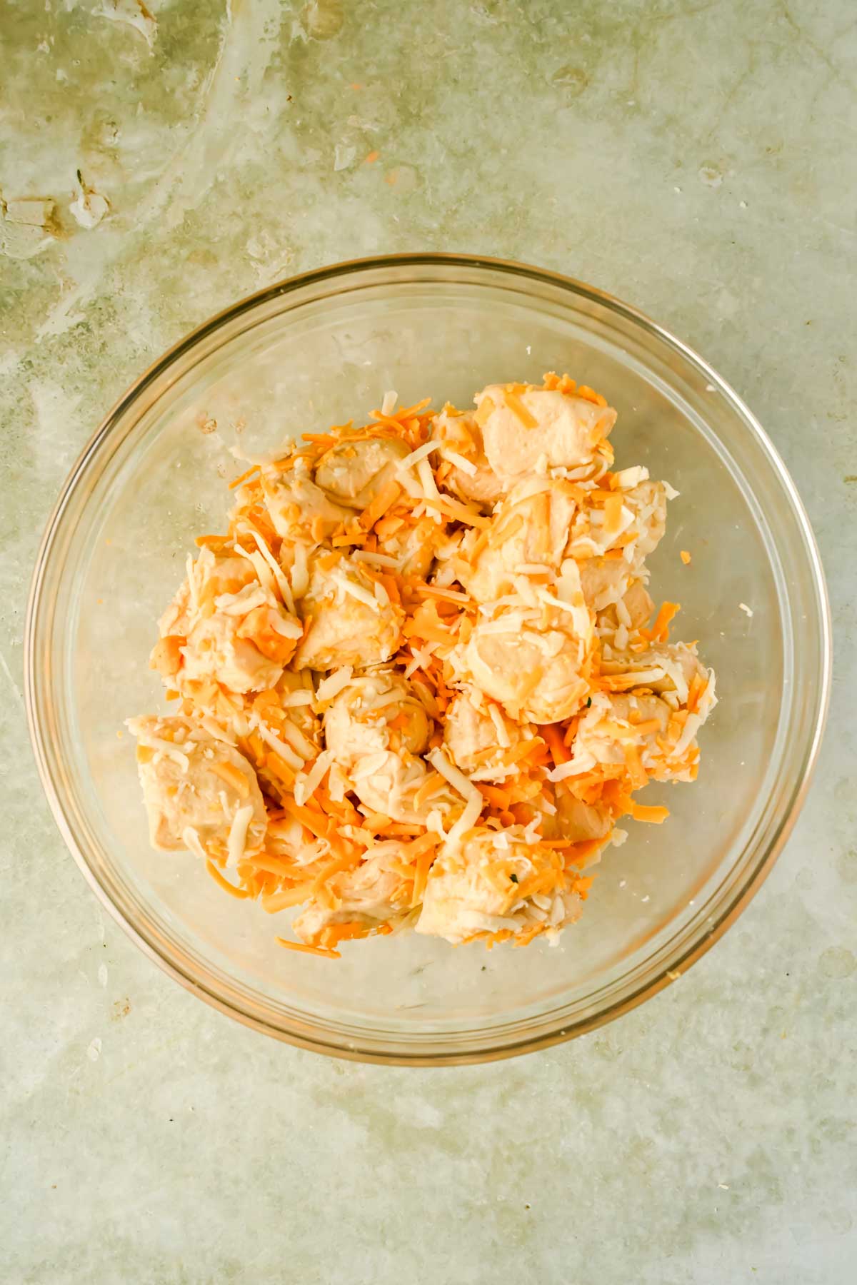 raw biscuit pieces with shredded cheese in glass mixing bowl.