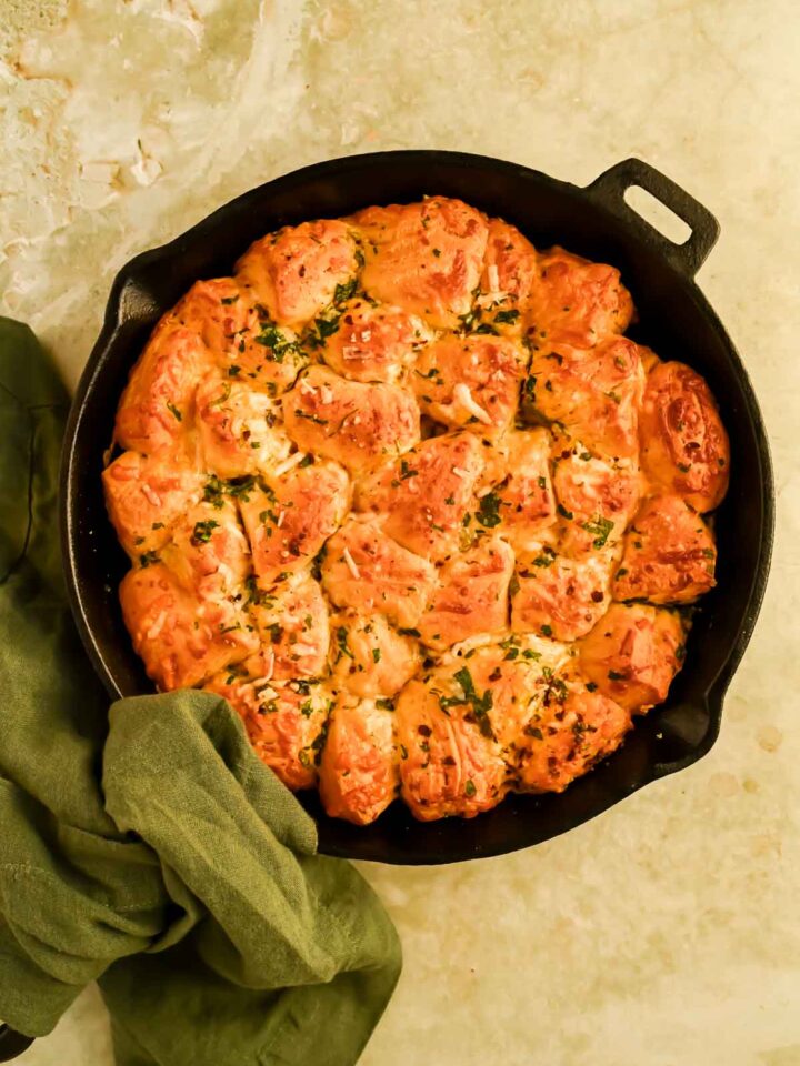 cheesy monkey bread garnished with fresh herbs in black skillet.