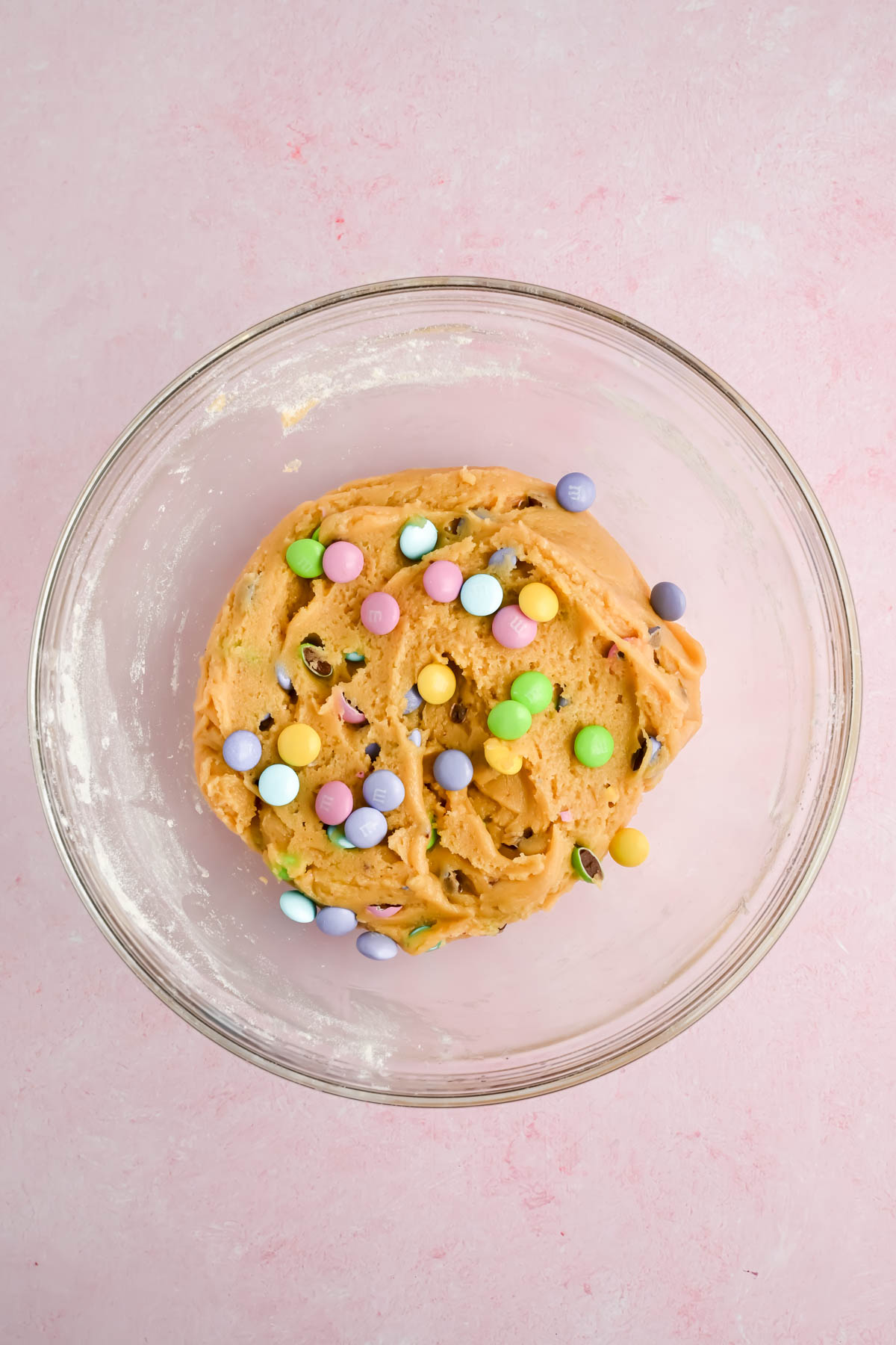 raw cookie dough with pastel m&m's added in glass mixing bowl.