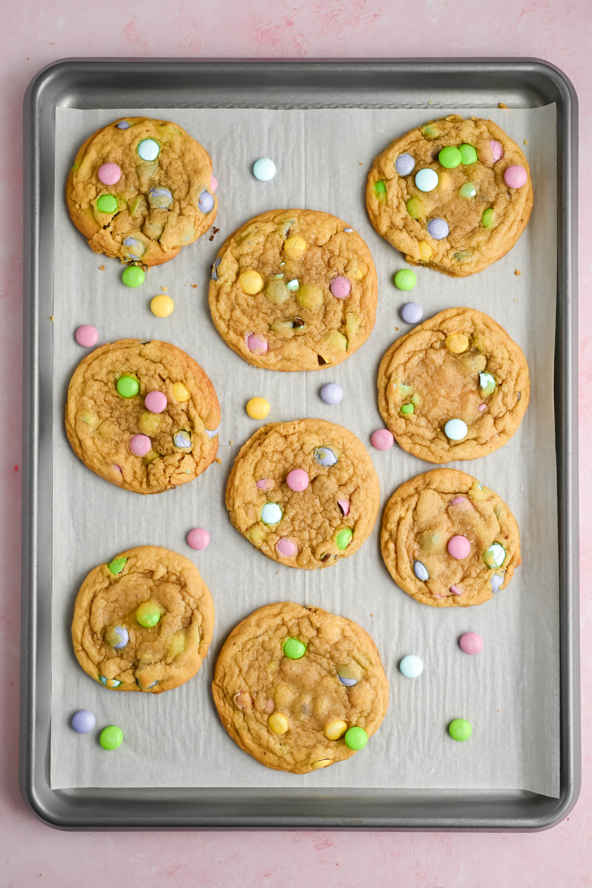 8 baked easter M&M cookies on parchment lined baking sheet.