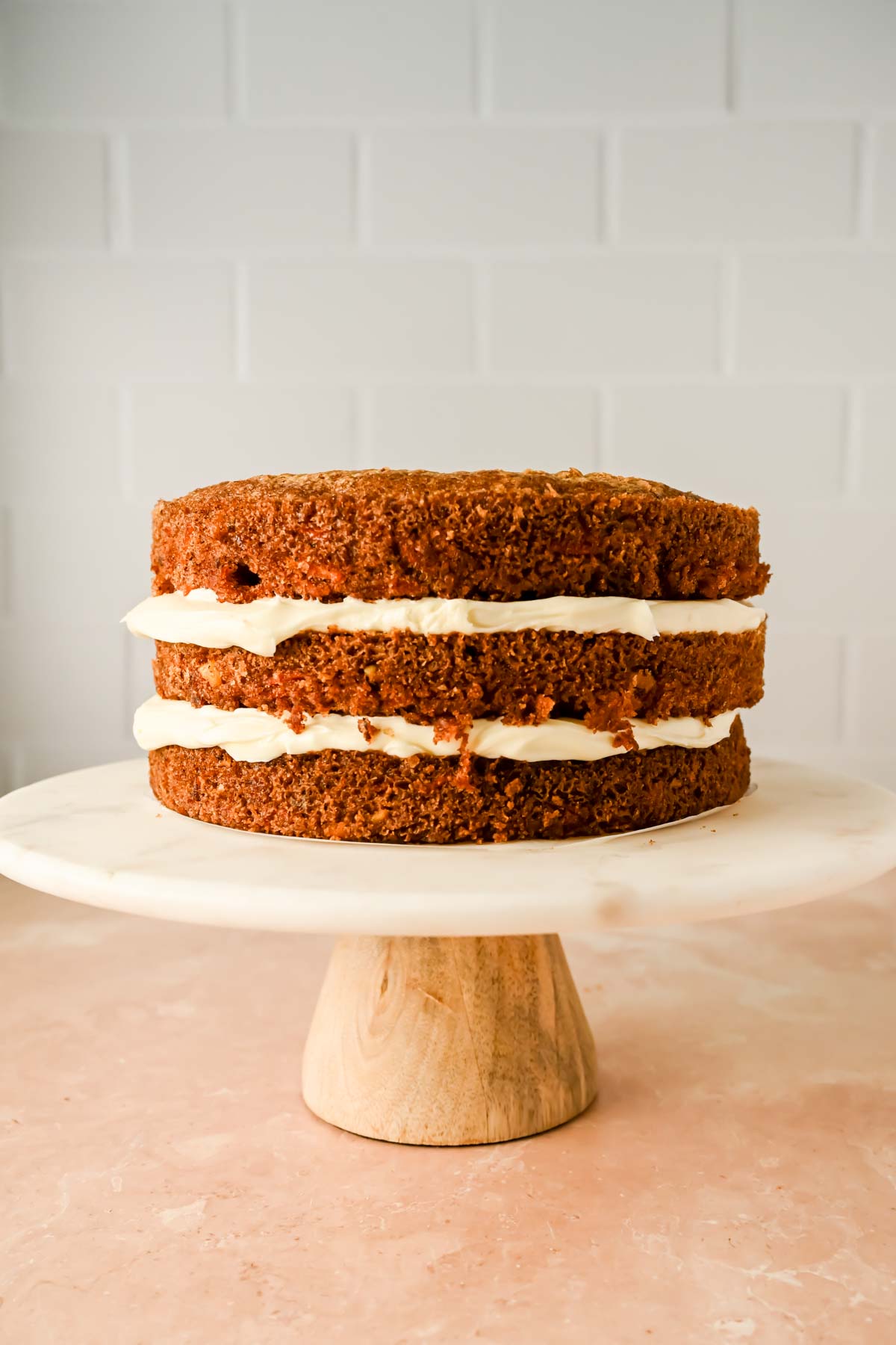 three layered carrot cake frosted between layers on marble cake stand. 